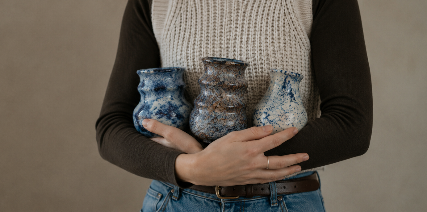 Person holding three ceramic pots against a plain background